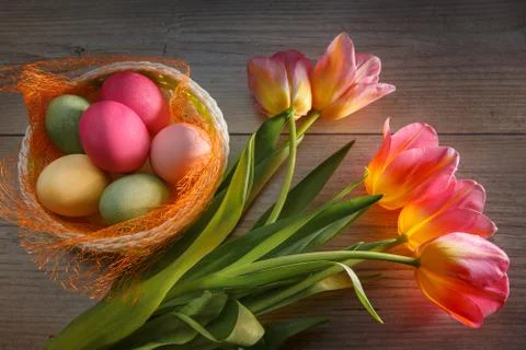 Multi-colored Easter eggs in a beautiful basket and a bouquet of tulips. Foto stock