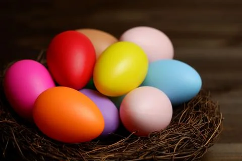 Multi colored easter eggs in birds nest on dark wooden planks table closeup 스톡 사진