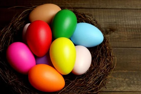 Multi colored easter eggs in birds nest on dark wooden planks table top view 스톡 사진