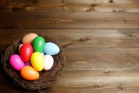Multi colored easter eggs in birds nest on dark wooden planks table 스톡 사진