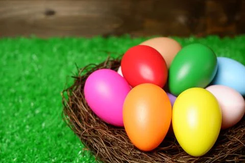 Multi colored easter eggs in birds nest on green grass and wooden planks Stock Photos