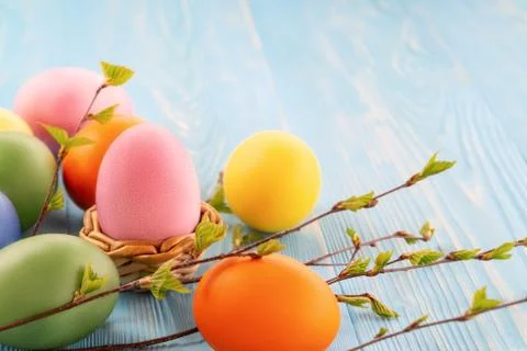 Multi-colored Easter eggs on a blue wooden table with twigs of birch with you Stock Photos
