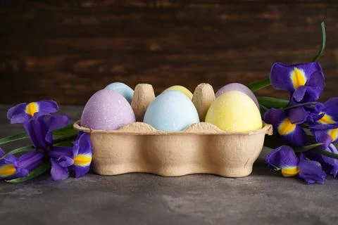 Multi colored Easter eggs in a cardboard box and fresh flower on a wooden bac Foto stock