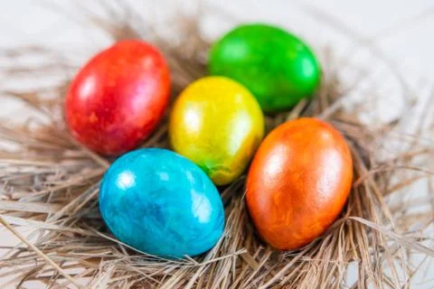 Multi-colored Easter eggs lie together on a straw in the form of a nest on a  Stock Photos