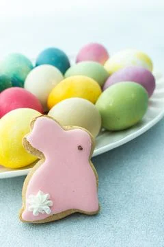 Multi-colored Easter eggs in an oval dish with decorative bunnies on a blue b Stock Photos