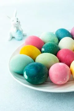 Multi-colored Easter eggs in an oval dish with decorative bunnies on a blue b Stock Photos