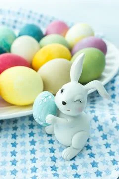 Multi-colored Easter eggs in an oval dish with decorative bunnies on a blue t Stock Photos
