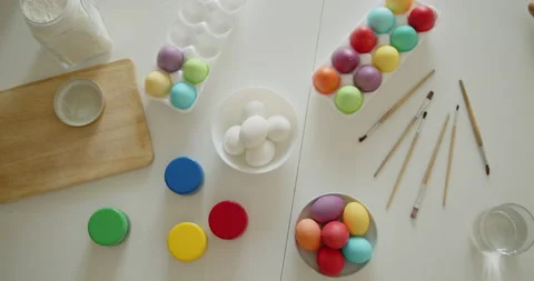 Multi-colored easter eggs, paint jars and brushes on a kitchen table top view Stock Footage 236794812