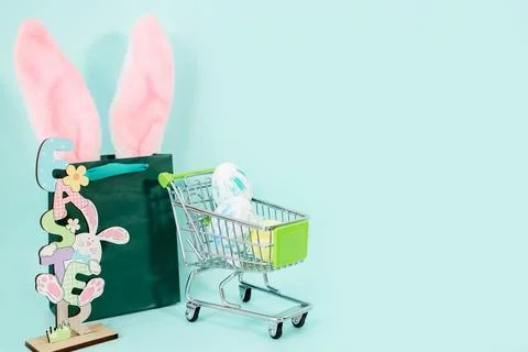 Multi-colored Easter eggs in a shopping cart, a green bag with rabbit ears Stock Photos