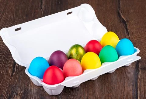 Multi-colored Easter eggs in a white plastic package on a wooden background. Stock Photos