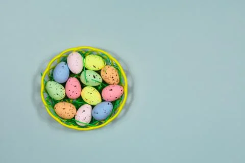 Multi-colored Easter eggs in a yellow basket on a blue background. Place for an Stock Photos