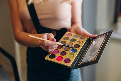 Multi-colored eyeshadow palette close-up. Makeup artist taps the eyeshadow with Stock Photos
