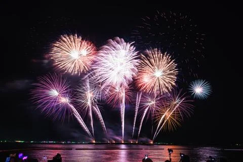Multi-colored Fireworks Exploding Over Calm Sea With Silhouetted Spectators.. Stockfoto's