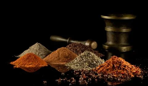 Multi-colored heaps of spices and a bronze mortar on a black mirror backgroun Stock Photos