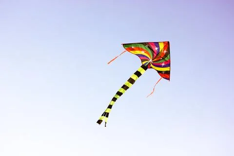 A multi-colored kite flies in a wind in the sky. Kid's entertainment, summer fun Stock Photos
