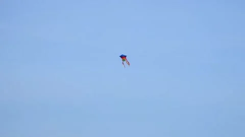 A multi-colored kite with ribbons flies from the wind in the blue autumn sky Stock Footage 164839600