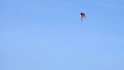 A multi-colored kite with ribbons flies from the wind in the blue autumn sky Stock Footage 166120227