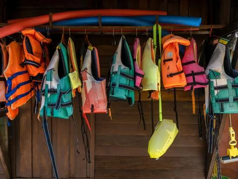 Multi-colored life jacket vests are hung on rail on wood wall for resort gu.. Stock Photos