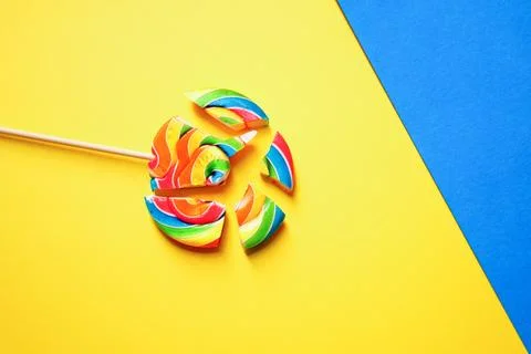 A multi-colored lollipop is split into pieces. The background is two colors Foto stock