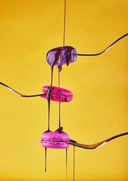 Multi-colored Macaron on forks with chocolate flowing from above on a yellow  Fotos Stock