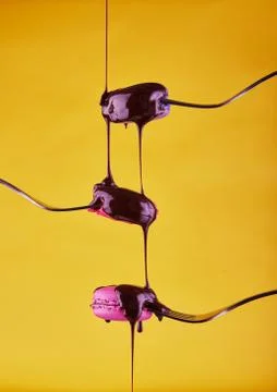 Multi-colored Macaron on forks with chocolate flowing from above on a yellow  Fotos Stock