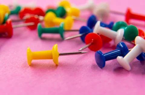 Multi-colored office buttons are scattered randomly on the pink surface Stock Photos