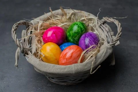 Multi-colored painted Easter eggs in a basket on a dark stone background. 写真素材