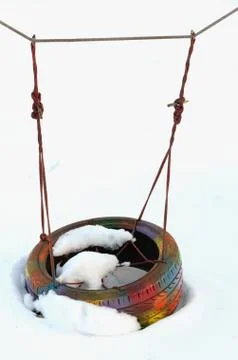 Multi-colored painted tire swing hanging by a rope of hemp in park covered in Stock Photos