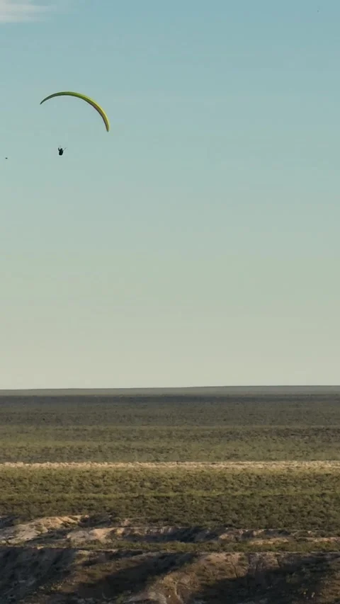 Multi colored paraglider flying in circles above desert plain area of big c.. Stock Footage 285146131