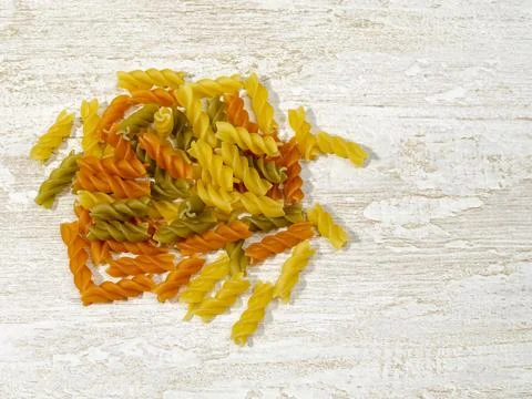 Multi-colored pasta scattered on the kitchen table. Stock Photos