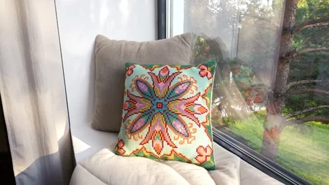 A multi-colored patterned pillow lies on a blanket on a windowsill at home Stockbeeldmateriaal 279270421