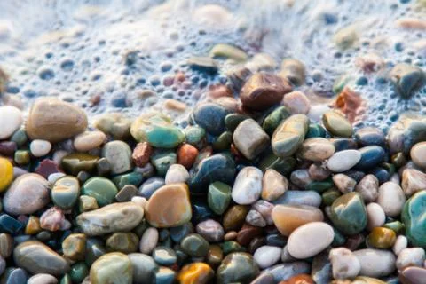 Multi-colored pebbles on the beach, washed by waves Stock Photos