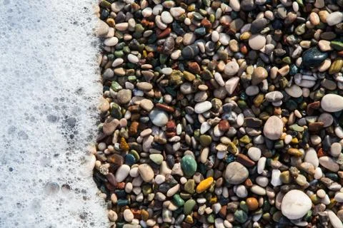 Multi-colored pebbles on the beach, washed by waves Stock Photos