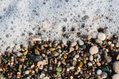 Multi-colored pebbles on the beach, washed by waves Stock Photos