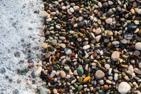 Multi-colored pebbles on the beach, washed by waves Stock Photos