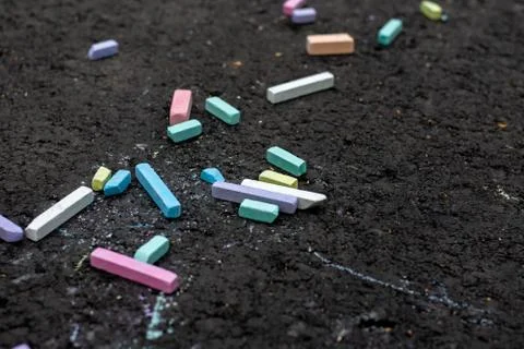 Multi-colored pieces of chalk lie on the black asphalt. Stock Photos