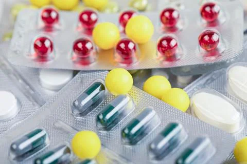 Multi-colored pills and capsules lie on the table. Scattered drugs. Stock Photos