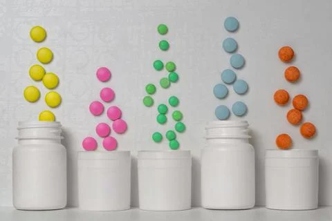 Multi-colored pills fly out of five white plastic jars Stock Photos
