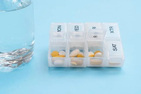 Multi-colored pills in a plastic box by days of the week and water for taking Stock Photos