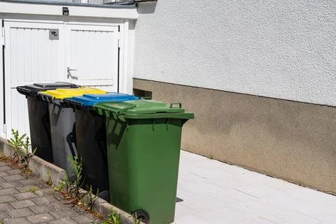 Multi-colored plastic bins for separate waste collection near the garage. Stock Photos