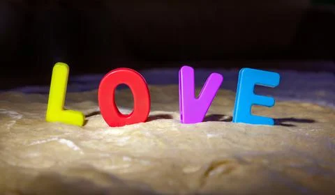 Multi-colored plastic letters stand among fresh dough and make up the word Love Stock Photos