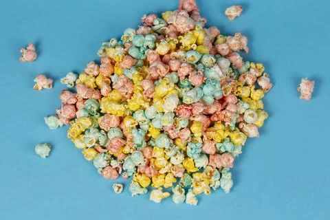 Multi-colored popcorn is scattered on a blue background. Colorful beautiful s Stock Photos
