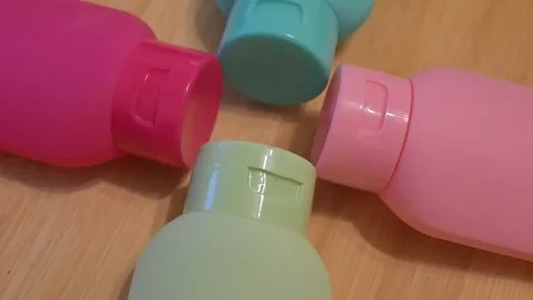 Multi-colored refillable travel bottles moving in circle on table, sustainable l Stock Footage 335280238