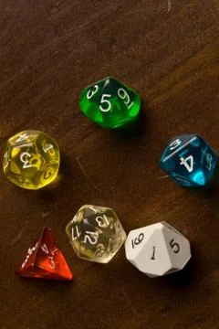 Multi-colored role play dice sitting on a wooden table top Stock Photos