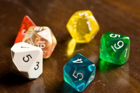 Multi-colored role play dice sitting on a wooden table top Stock Photos
