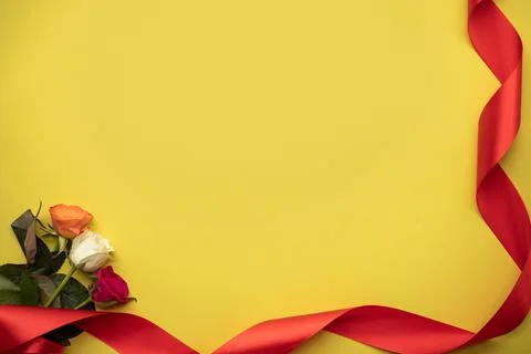 Multi-colored roses on a yellow background with a red ribbon. place for text Stock Photos