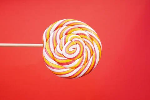 Multi-colored round lollipop on a bright red background. Close up. Stock Photos