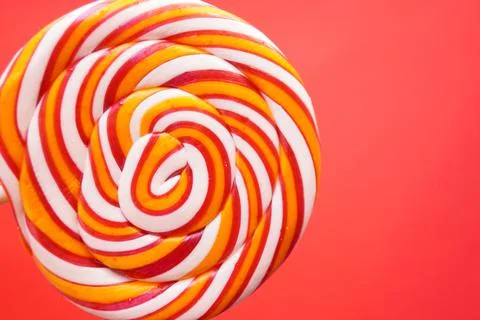 Multi-colored round lollipop on a bright red background. Close up. Stock Photos