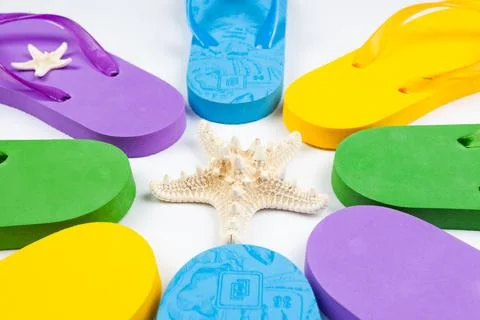 Multi-colored rubber beach flip flops around the starfish on a white background Stock Photos