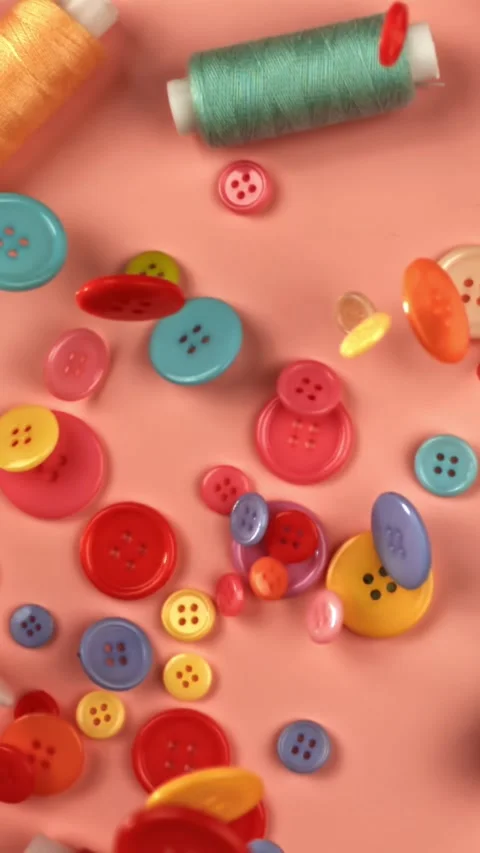 Multi-colored sewing buttons fall on a red table. Filmed on a high-speed camera Stock Footage 335372356